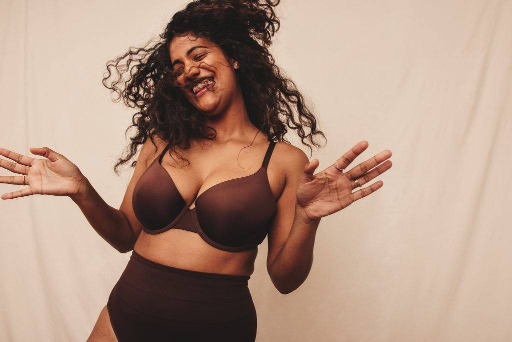 Filled with happiness and positive vibes. Happy young woman laughing cheerfully while standing against a studio background. Body positive young woman embracing her natural self.